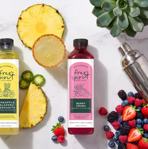 Pineapple Jalapeño Margarita and Berry Crush bottles on marble with fresh pineapple, jalapeño, strawberries, blackberries, and blueberries